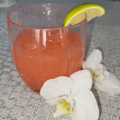 Refreshing Frozen Cocktail of Grapefruit, Vodka, Triple Sec, and Campari with white orchid next to it and a lime slice