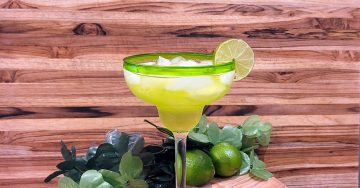 green drink in a margarita glass garnished with a lime in front of a wood background and limes