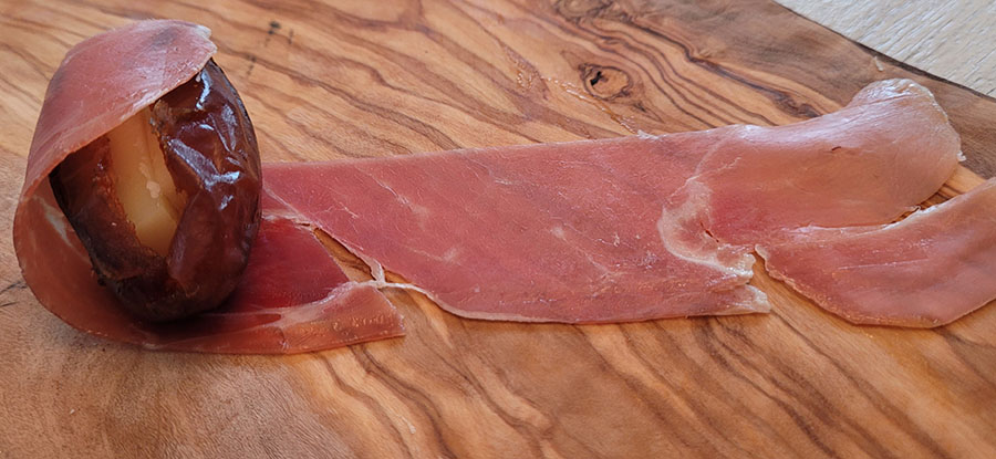 slice of proscuitto being wrapped around a date