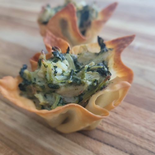 artichoke spinach and chicken in a creamy cheese sauce sitting in a wonton wrapper bowl