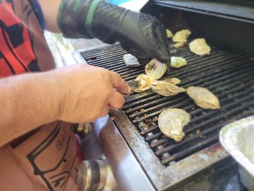 man shucking oysters on a grill