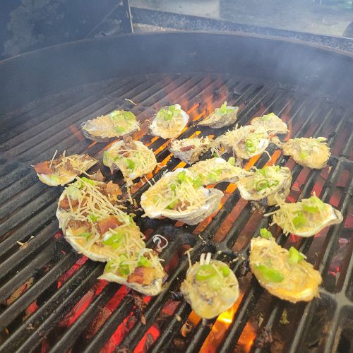 oysters on the grill with toppings of green onion, and bacon