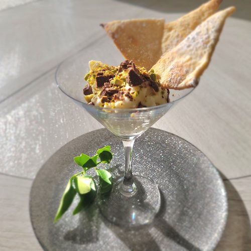 almond flavored canoli filling piped into a martini glass with crushed patachios and chocolate shavings with pastry chips