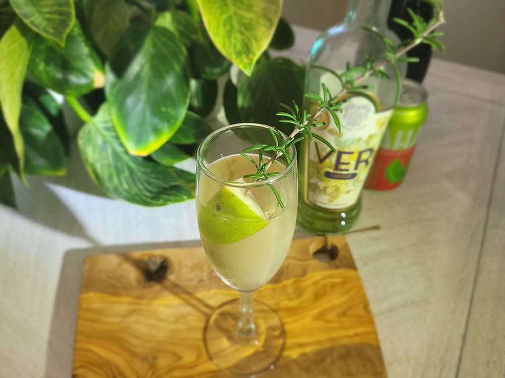champagne glass with prossecco, Ver liqueur, ginger soda garnished with an apple and sprig of rosemary