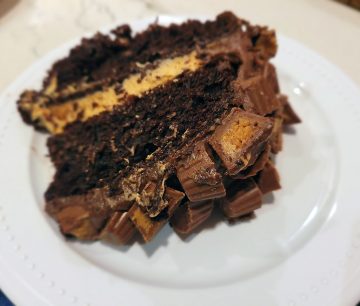 Slice of layered chocolate cake with a light brown peanut butter flavored filling and topped with Reeses Peanut Butter Cup Candies