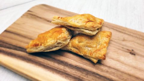 Curry puff pastry bites stacked on a wooden board