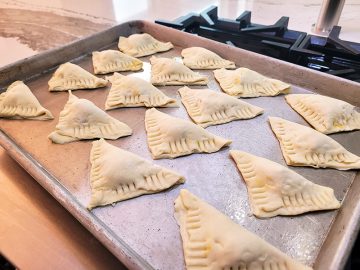 uncooked puff pastry triangles with fork pinched edges on a cookie sheet