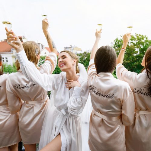 Happy Bachelorettes in wedding silk robes toasting the bride