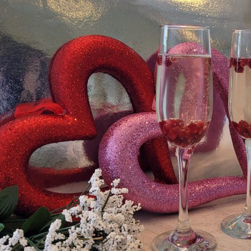 champagne flutes with champagne and pomegranate with heart in the background