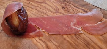 slice of proscuitto being wrapped around a date