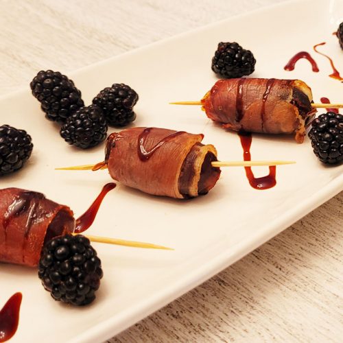 3 prosciutto wrapped appetizers on a white plate with blackberry garnishes