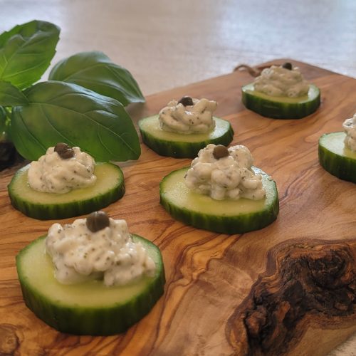Cucumber bites with cheese and a caper on a wooden board