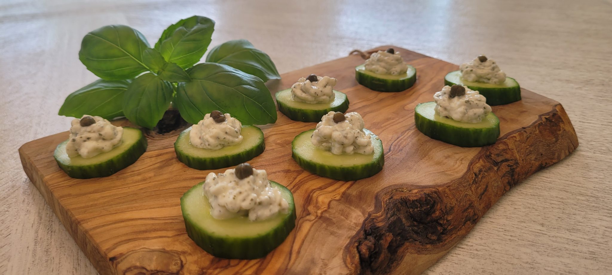 Cucumber bites with cheese and a caper on a wooden board