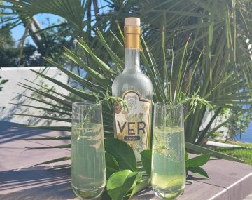 VER liqueur in front of palms. There are also two cocktails with rosemary garnish