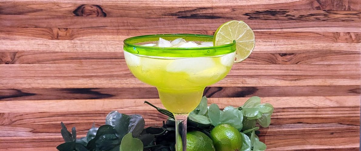 green drink in a margarita glass garnished with a lime in front of a wood background and limes