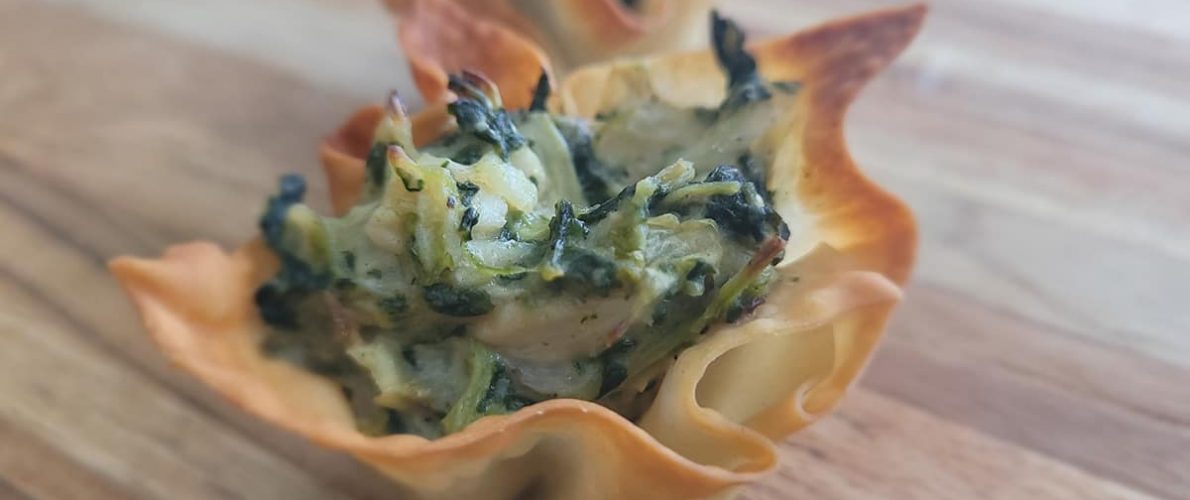 artichoke spinach and chicken in a creamy cheese sauce sitting in a wonton wrapper bowl