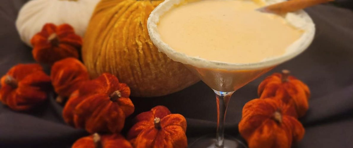 pumpkin spice martini sits in front of straw pumpkin decorations